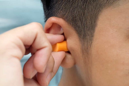 Man puts orange earplug in ear